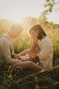 a man and woman are sitting in the grass with their newborn baby, who is being held by her