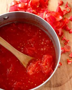 a wooden spoon in a pot filled with tomato sauce and chopped red peppers on the side