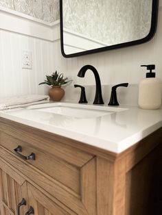 a bathroom sink with two faucets and a mirror above it, next to a plant