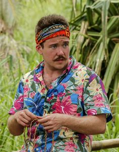 a man with a flowered shirt and tie around his head sitting on a bench