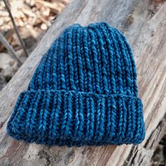 a blue knitted hat sitting on top of a wooden log