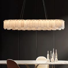 a modern chandelier hanging over a dining table with chairs and bottles on it