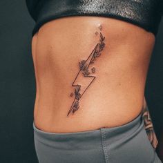 a woman's lower back tattoo with flowers and lightning bolt on her left side