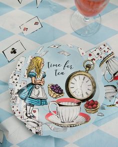 a plate with alice in wonderland on it next to a glass of wine and some cards