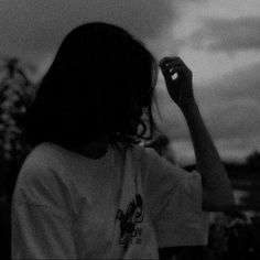 a woman standing in front of a cloudy sky with her hand up to her face