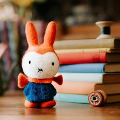 a small stuffed animal sitting next to a stack of books on a wooden table in front of a pile of books