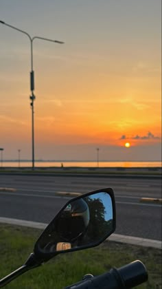 the sun is setting behind a motorcycle's side mirror