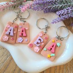 three keychains with letters and stars on them sitting next to purple flower stems