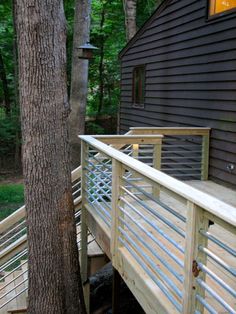 a wooden deck next to a tree in front of a black house with white railings