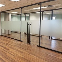 an empty room with glass partitions and wood flooring in front of the windows