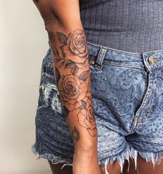 a woman's arm with roses tattooed on it and ripped denim shorts in front of her