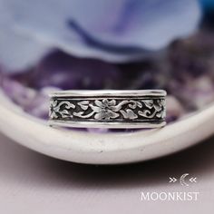 a close up of a silver ring on a purple flowered background with the words moonkist above it