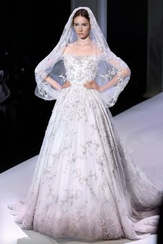 a woman in a white wedding dress on the catwalk wearing a veil and tiara