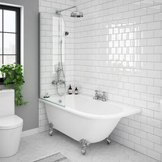 a white bath tub sitting next to a toilet in a bathroom under a window with potted plants