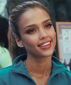 a close up of a person wearing a necklace and smiling at the camera with other people in the background