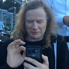 a man with long hair is looking at his cell phone and then he's taking a selfie