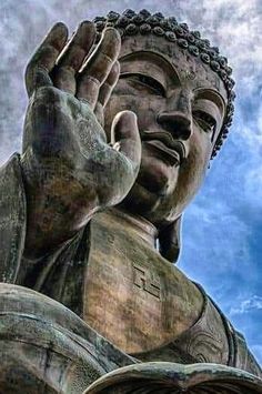 there is a large buddha statue with his hands up in the air and clouds behind him