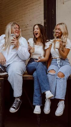 three women sitting on a bench drinking coffee and eating doughnuts with their mouths open