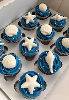 blue and white cupcakes with seashells on them are in a box