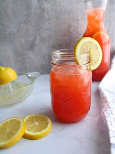 two mason jars filled with lemonade sit on a marble counter next to sliced lemons