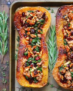 two delicacy squash halves on a baking sheet with fresh herbs and walnuts