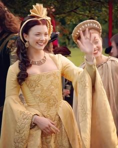 two women dressed in period costumes wave at the camera while standing next to each other