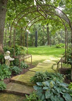 a garden area with stone steps, trees and plants in the foreground is an iron arbor