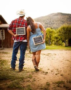 a man and woman walking down a dirt road with signs in their hands that read, i love you