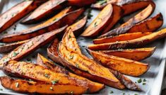 baked sweet potato wedges on a baking sheet with herbs sprinkled on top