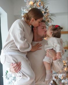 a woman holding a baby and kissing her face in front of a christmas tree with lights