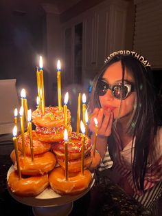 a woman is blowing out candles on a doughnut cake with many donuts in front of her