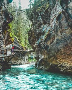 a person standing on a bridge over a river in the middle of some rocks and trees