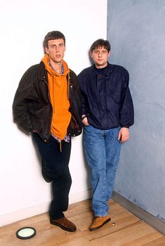 two men standing next to each other in front of a wall