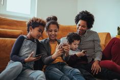 three adults and two children sitting on a couch looking at a cell phone together,