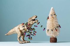 two toy dinosaurs standing next to a christmas tree