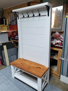 a wooden bench sitting in front of a white wall with hooks on it's side