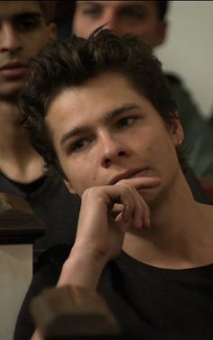 a young man sitting in front of other men at a table with his hand on his chin