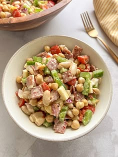 a white bowl filled with salad next to a wooden spoon and fork on top of a table