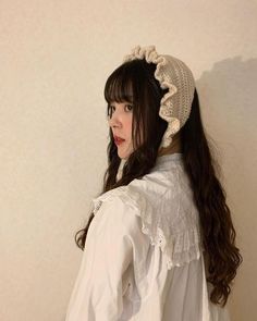 a woman with long dark hair wearing a white shirt and a crochet hat