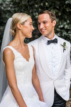 a bride and groom standing next to each other in front of some greenery at their wedding