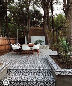 an outdoor dining area with black and white tiles on the floor, wooden fence and trees