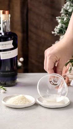 a person is pouring something into a bowl on a table next to a bottle of wine