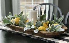 a wooden tray filled with lemons and greenery on top of a dining room table