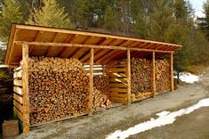 several stacks of logs stacked on top of each other in front of some trees and snow