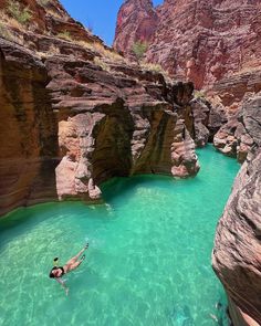 a person swimming in the water near some rocks and cliffs with blue green colored water