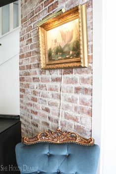 a blue chair sitting in front of a painting on a brick wall next to a piano