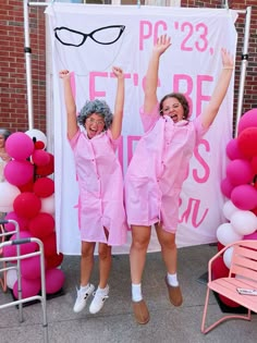 two women in pink outfits standing next to a sign