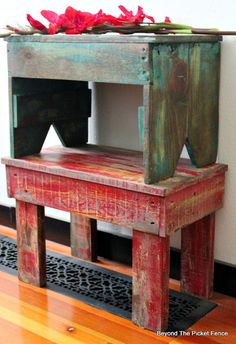 a wooden bench with red flowers on top and black metal grate under the bench