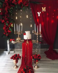 a red and white wedding cake surrounded by candles, flowers and other decorations on a table