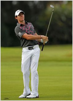 a man holding a golf club while standing on top of a green covered golf course